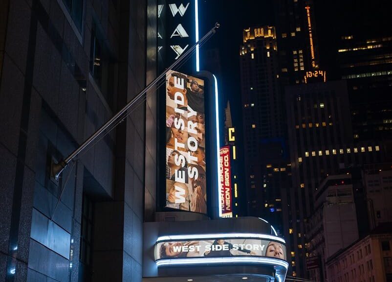 A vibrant night view of Broadway Theater in New York City featuring West Side Story signage.