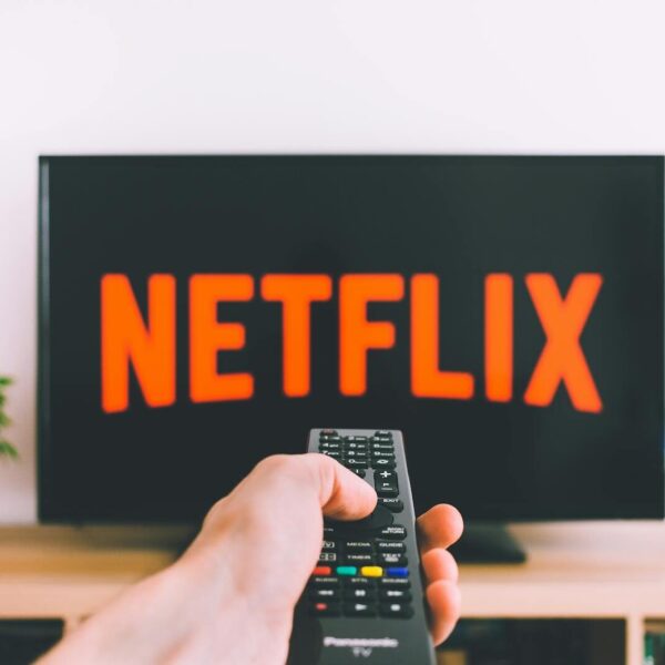A hand holding a TV remote in front of a screen with Netflix, perfect for streaming and movie night themes.