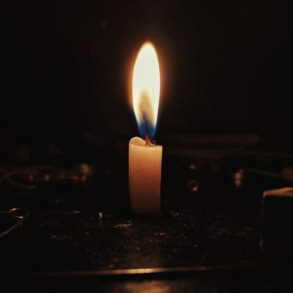 A single candle flame casting a warm glow in a dark, contemplative setting.