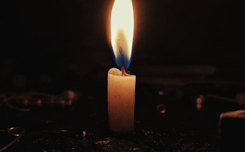 A single candle flame casting a warm glow in a dark, contemplative setting.
