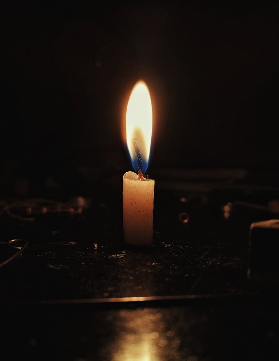 A single candle flame casting a warm glow in a dark, contemplative setting.