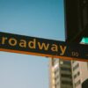 A vibrant street sign depicting Broadway during twilight with a city backdrop.