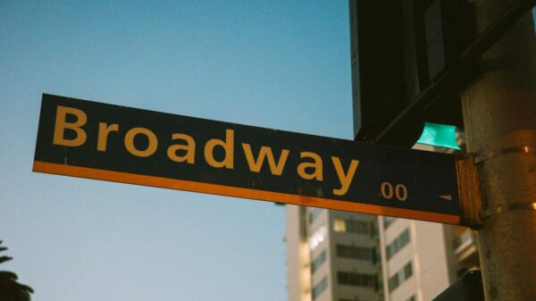 A vibrant street sign depicting Broadway during twilight with a city backdrop.