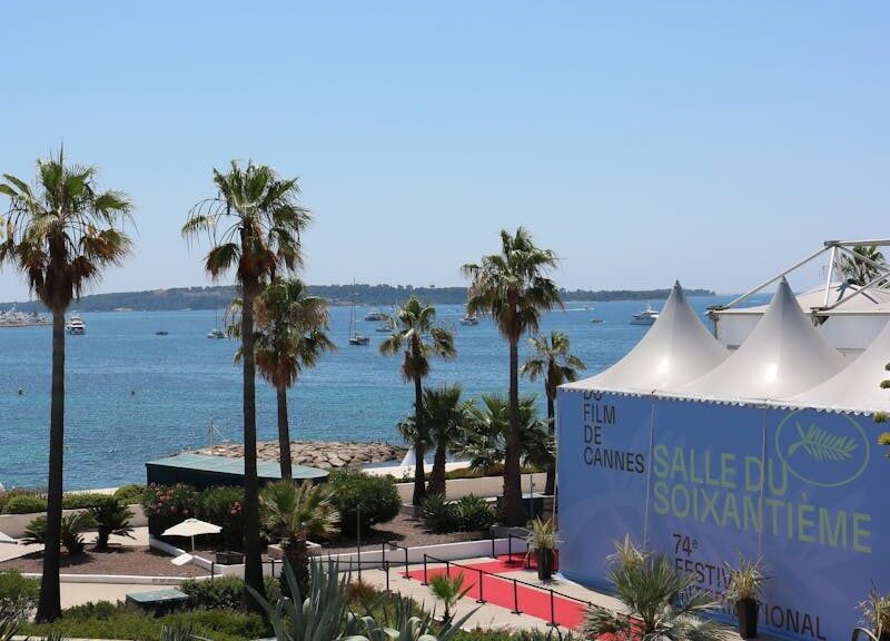A scenic view of Cannes Film Festival tents with a backdrop of the sea and palm trees.