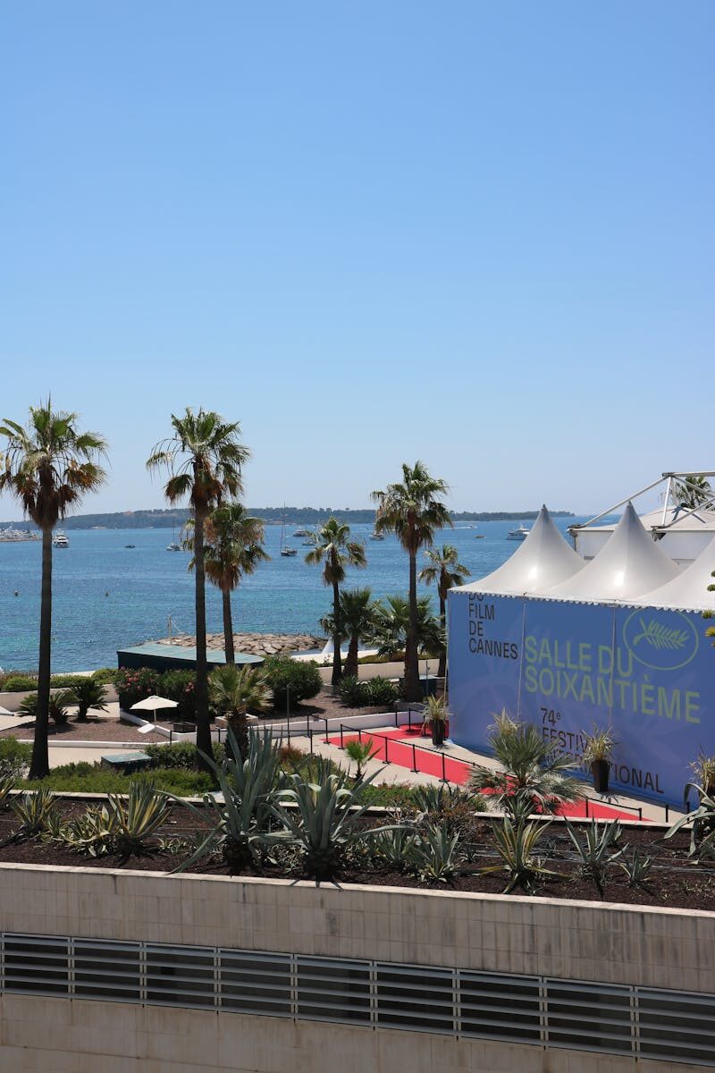 A scenic view of Cannes Film Festival tents with a backdrop of the sea and palm trees.