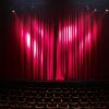 Empty theater stage with red curtains and seating, ready for a performance.
