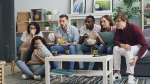 Group of friends watching a thriller movie at home, sharing snacks and reactions.
