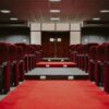 A luxurious empty auditorium with rows of red velvet seats and a red carpet aisle.