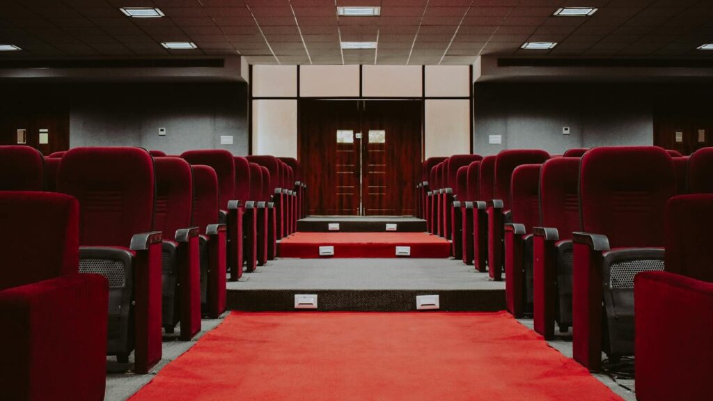 A luxurious empty auditorium with rows of red velvet seats and a red carpet aisle.
