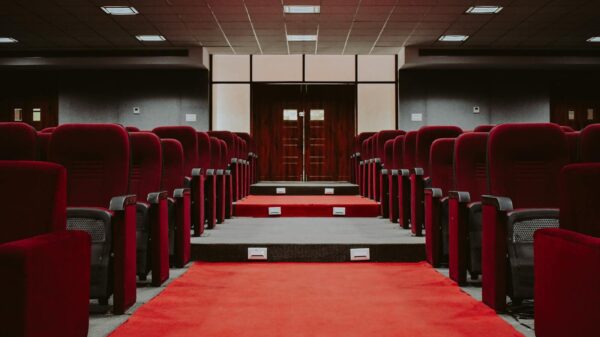 A luxurious empty auditorium with rows of red velvet seats and a red carpet aisle.