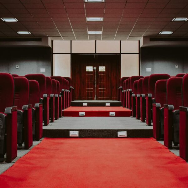 A luxurious empty auditorium with rows of red velvet seats and a red carpet aisle.