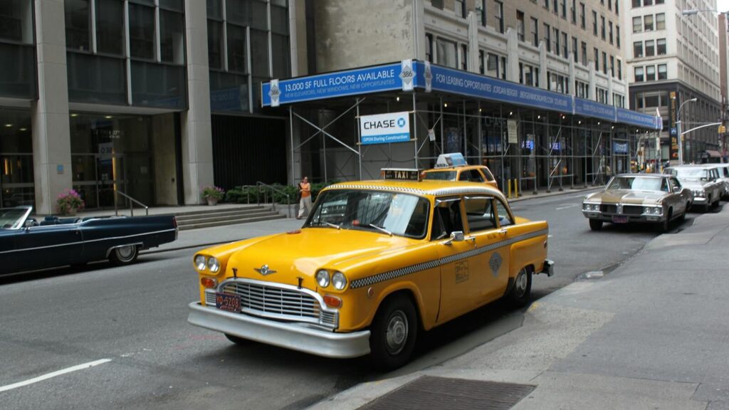 Vintage yellow taxi cab parked on a bustling New York City street.