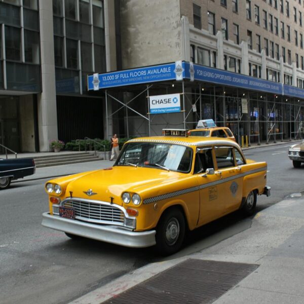 Vintage yellow taxi cab parked on a bustling New York City street.