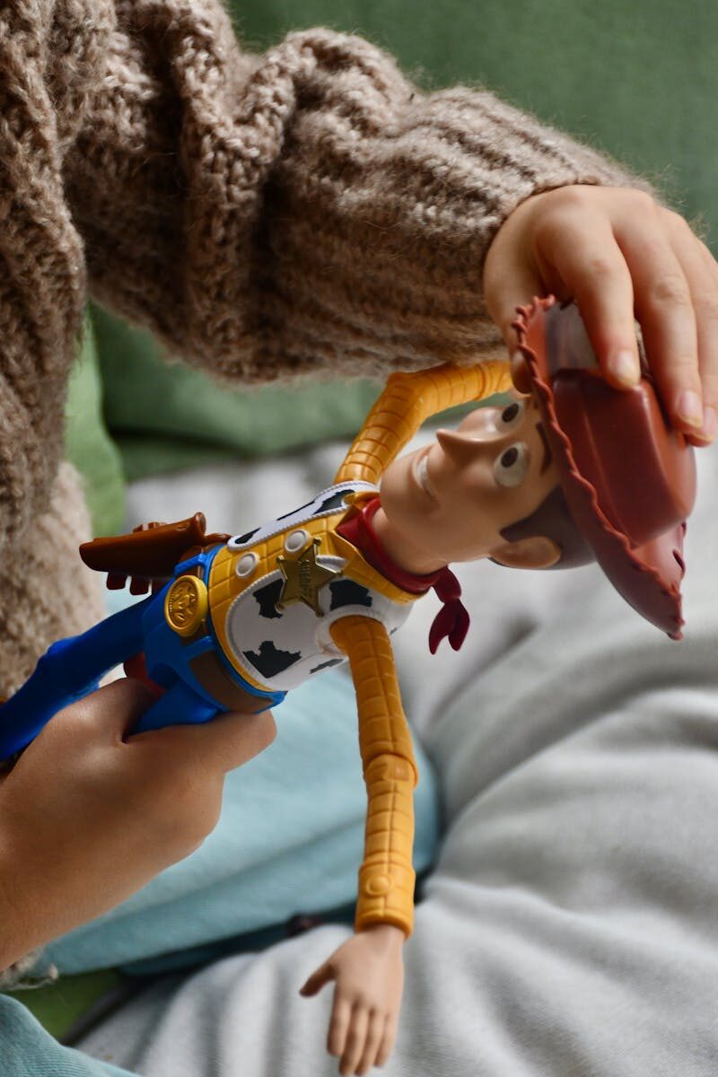 Child's hand holding a cowboy doll indoors, showing playtime fun.