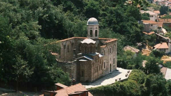 A picturesque view of a historic church in Prizren, Kosovo, amidst lush summer greenery.
