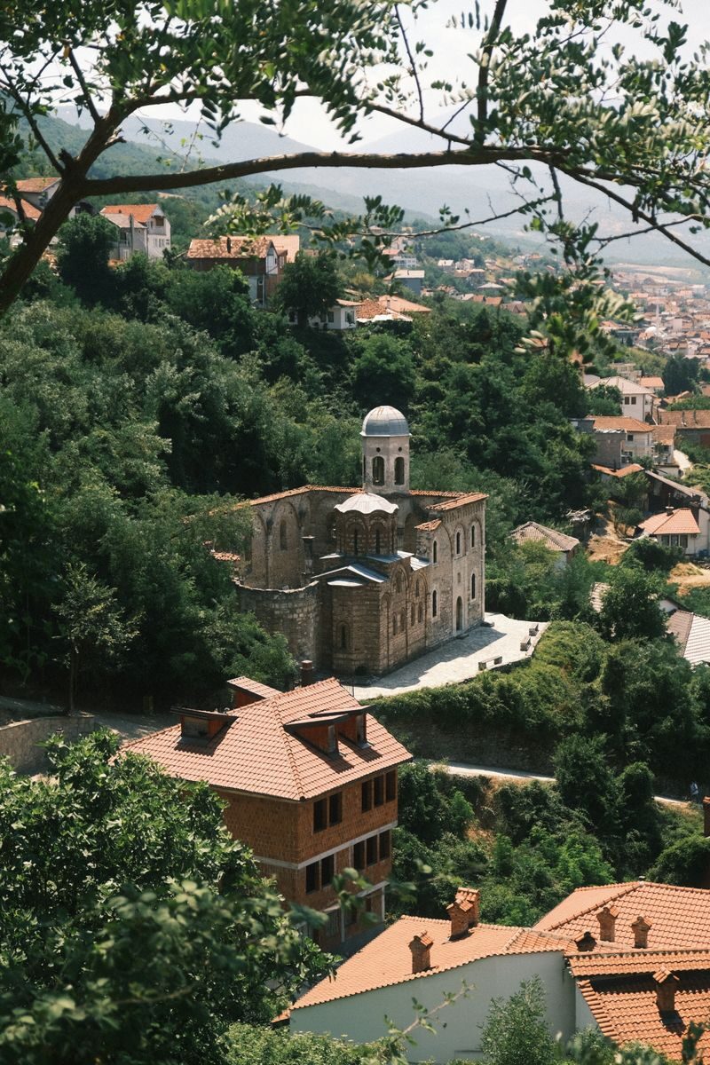 A picturesque view of a historic church in Prizren, Kosovo, amidst lush summer greenery.