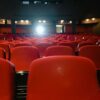 A view of an empty cinema with rows of red seats facing the illuminated screen.