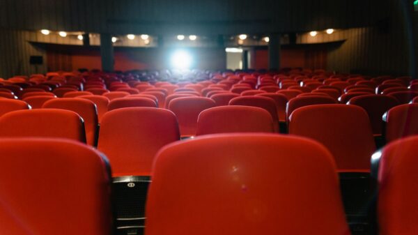 A view of an empty cinema with rows of red seats facing the illuminated screen.