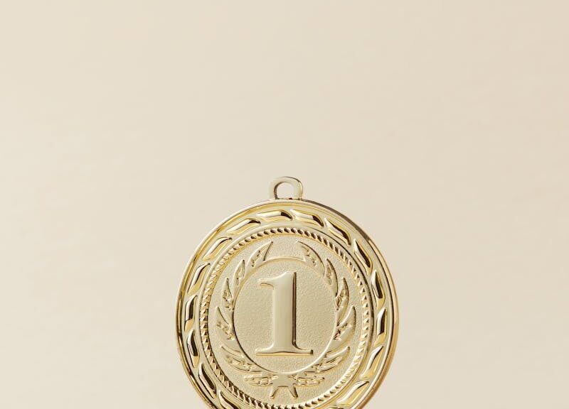Close-up of a gold medal with number one on beige background, symbolizing victory.