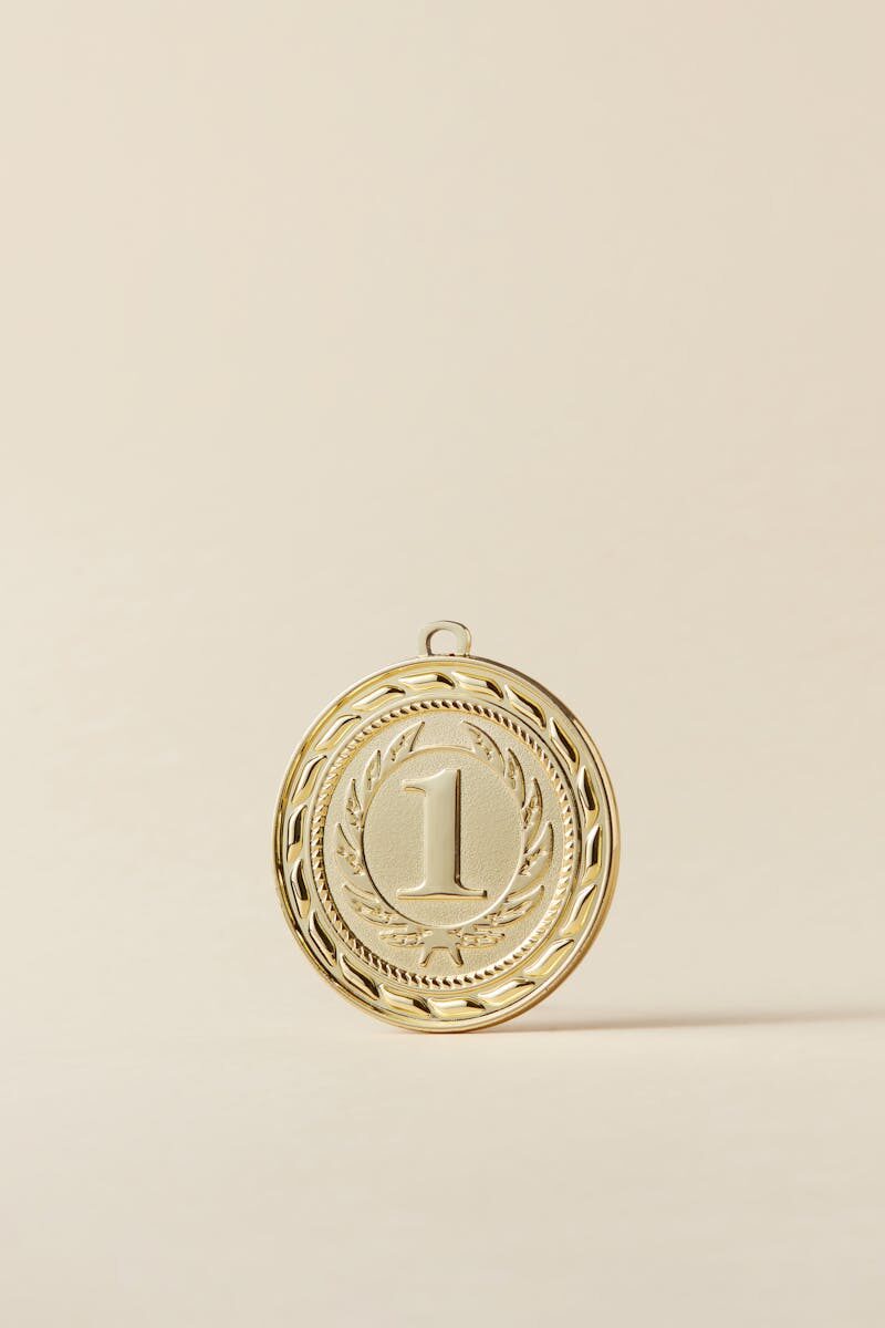 Close-up of a gold medal with number one on beige background, symbolizing victory.