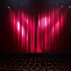 Empty theater stage with red curtains and seating, ready for a performance.