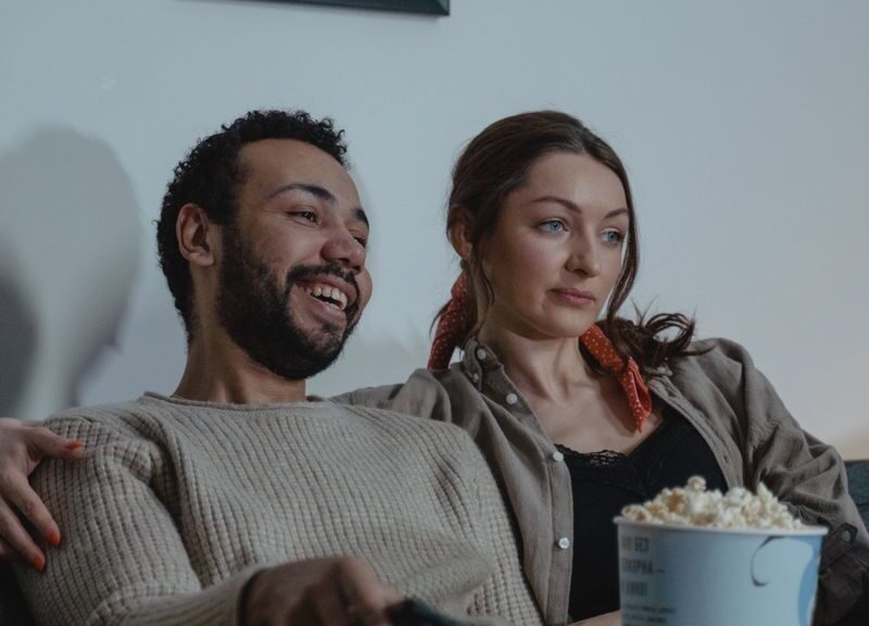 Smiling couple enjoying a cozy evening with popcorn and TV. Ideal for lifestyles imagery.
