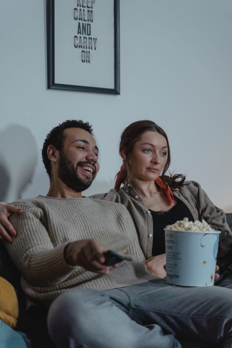 Smiling couple enjoying a cozy evening with popcorn and TV. Ideal for lifestyles imagery.