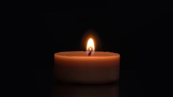 A single candle flame reflecting on a dark surface with a black background.