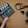 Top view of classic filmmaking tools including a slate and vintage camera on a cork surface.