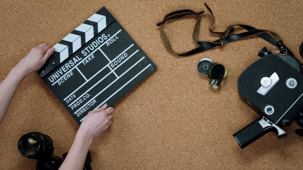 Top view of classic filmmaking tools including a slate and vintage camera on a cork surface.