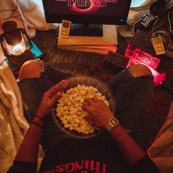 Person enjoying popcorn while watching Stranger Things in a cozy room setup.