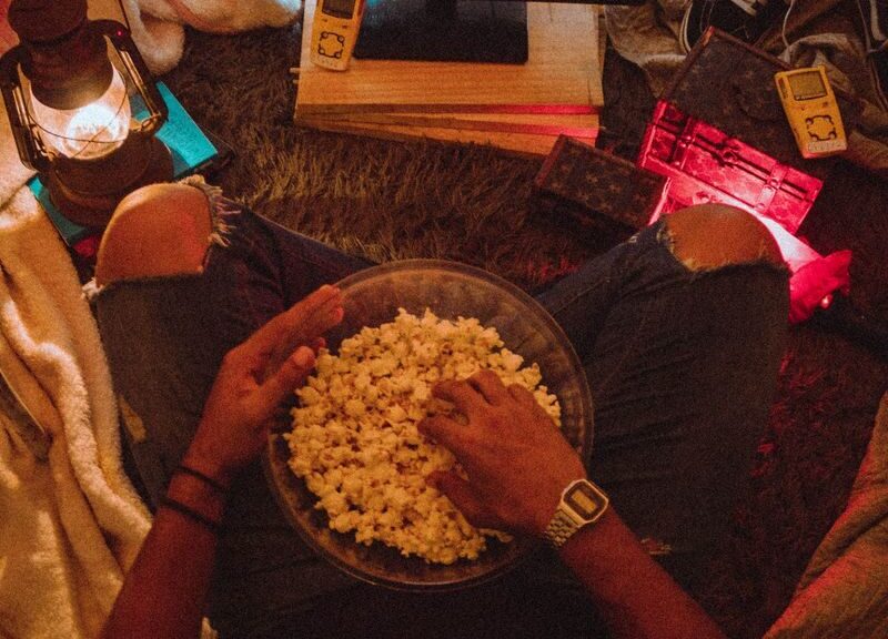Person enjoying popcorn while watching Stranger Things in a cozy room setup.