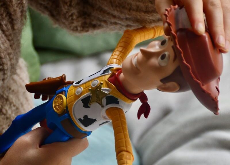 Child's hand holding a cowboy doll indoors, showing playtime fun.