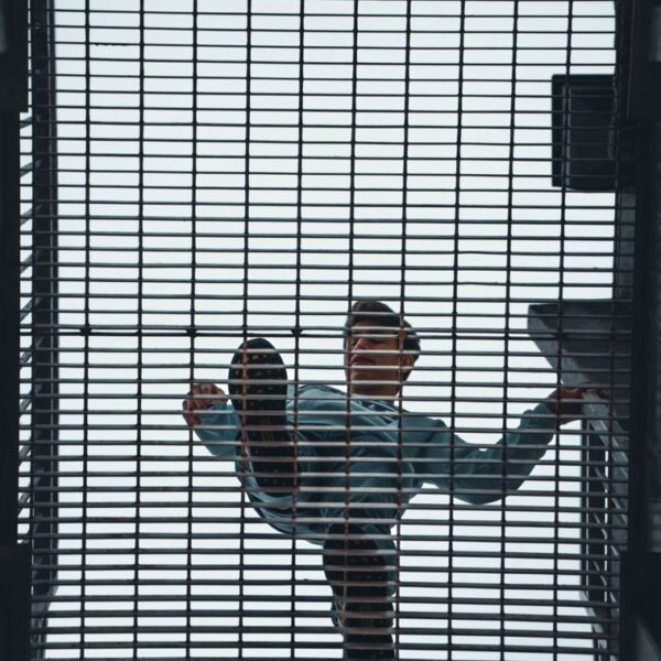 Man walking above a steel grate with geometric patterns, seen from below.
