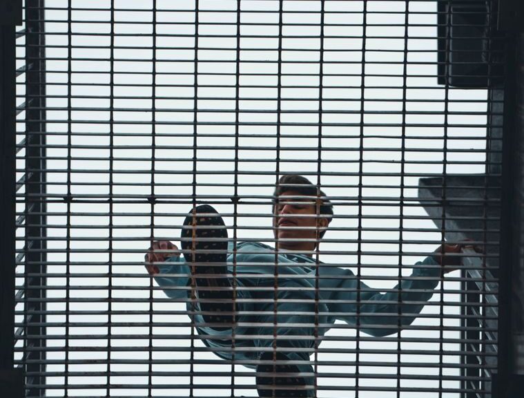 Man walking above a steel grate with geometric patterns, seen from below.