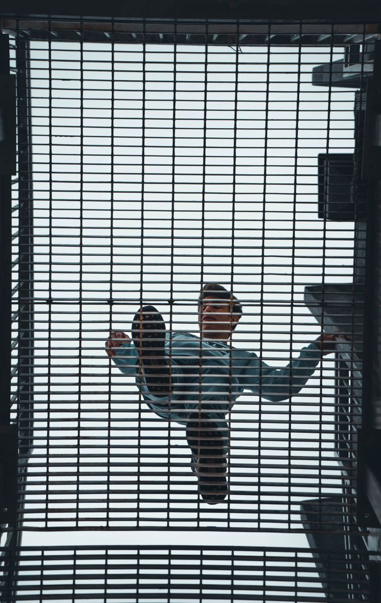 Man walking above a steel grate with geometric patterns, seen from below.