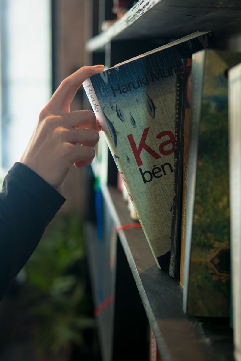 A hand reaches for a book on a shelf, bathed in soft lighting indoors.