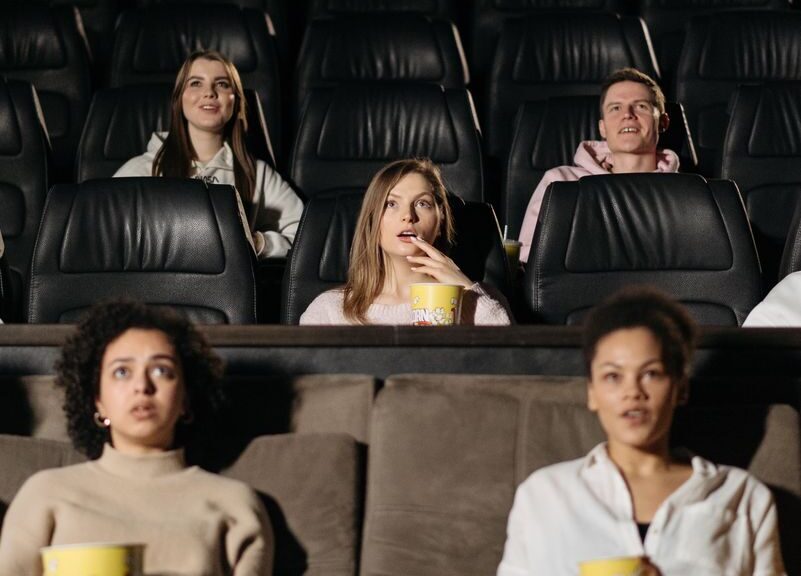 Audience watching film in theater, enjoying popcorn in a cozy setting.