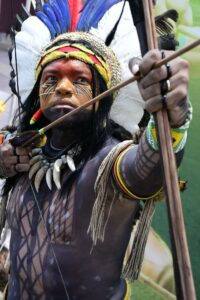 Portrait of an indigenous man with painted body and bow, showcasing cultural tradition.
