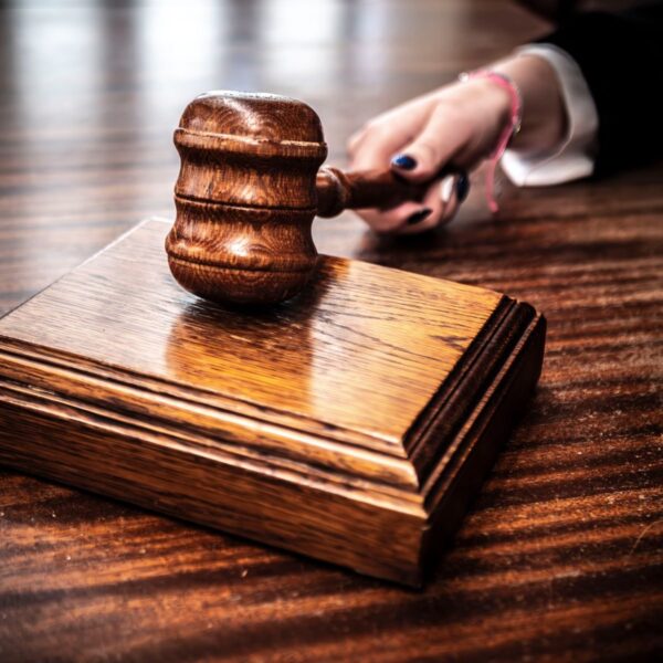 Close-up image of a wooden gavel held by hand on a desk in a courtroom setting.