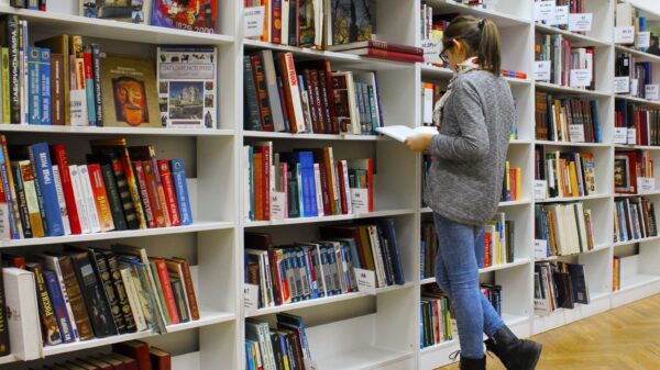 A young woman stands reading a book in a well-stocked library.