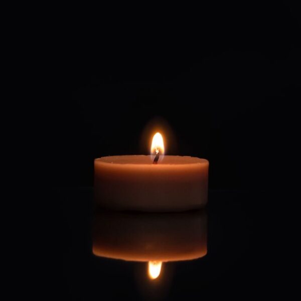 A single candle flame reflecting on a dark surface with a black background.