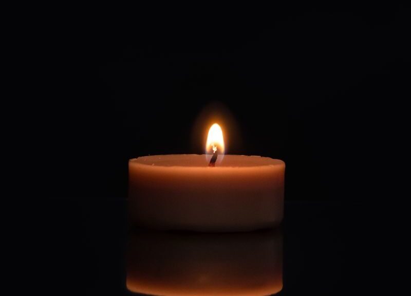 A single candle flame reflecting on a dark surface with a black background.