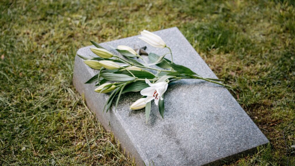 White lilies placed on a gravestone in a serene cemetery setting.
