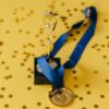 A golden trophy and medal with blue ribbon on a confetti-strewn yellow surface, symbolizing victory and achievement.