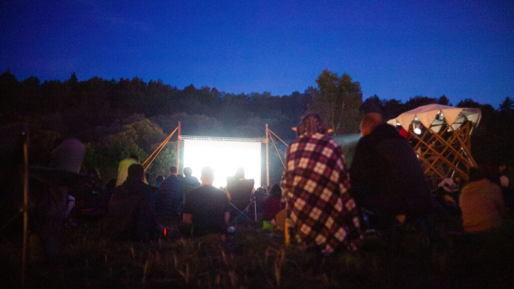 Adults gather outdoors for a night movie screening under the stars.