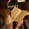 A young woman reading in front of a bookshelf filled with books, creating a warm, vintage feel.
