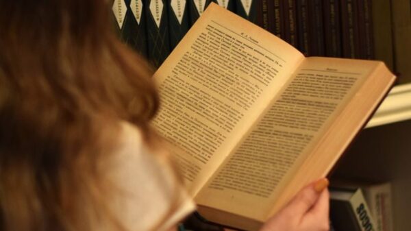 A young woman reading in front of a bookshelf filled with books, creating a warm, vintage feel.