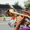 A man plays the trumpet outdoors during a lively festival parade.