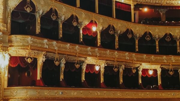 Luxurious opera house interior featuring ornate gold designs and red velvet balconies.